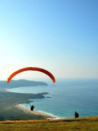 Person paragliding over sea against clear sky