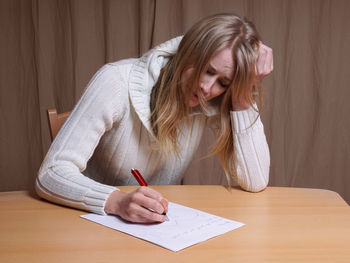 Sad young woman writing on paper while sitting on chair by table