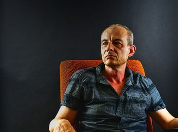 Thoughtful mature man sitting on chair against black wall