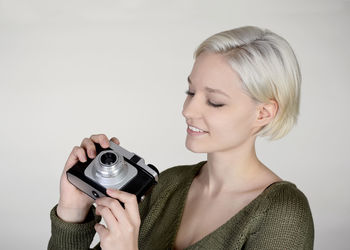 Portrait of smiling woman photographing against white background