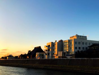 Buildings by river against clear sky during sunset