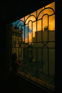 Rear view of silhouette man standing by building against sky during sunset