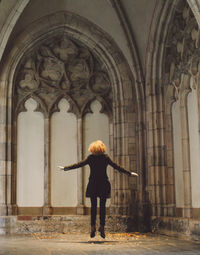 Rear view of young woman with arms outstretched jumping at church