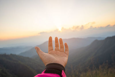 Cropped hand of woman gesturing against mountains and sky