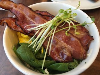 Close-up of baked bacon with sprouts and spinach in bowl on table