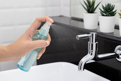 Close-up of hand holding faucet in bathroom