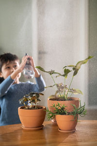 A boy sprays flowers in orange clay terracotta pots with a spray gun.