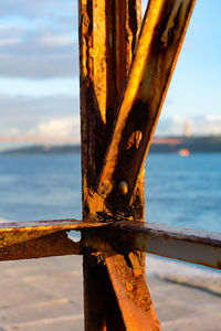 Close-up of rusty metal fence by sea against sky