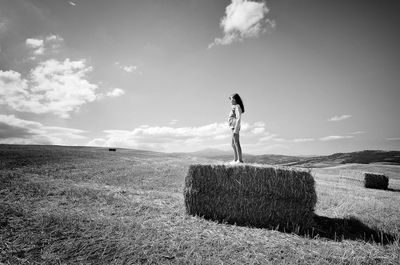 Full length side view of girl standing on hay at field against sky