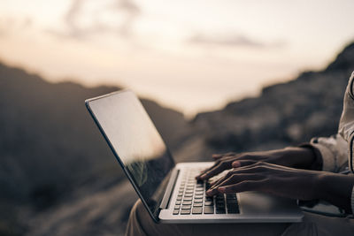 Hands of woman typing on laptop at sunset on vacation