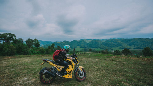 Man with motorcycle on field against sky