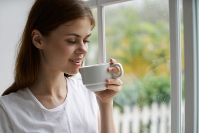 Young woman drinking coffee cup by window at home