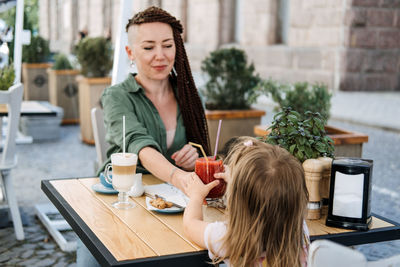 Mother and little daughter eating in the street cafe. trendy hipster mother with dreadlocks and