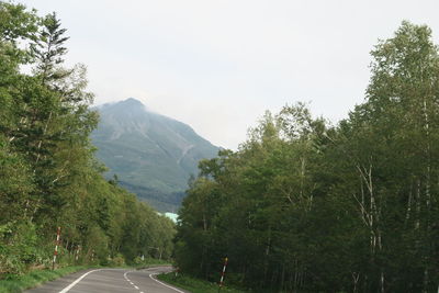 Road amidst trees and mountains against sky