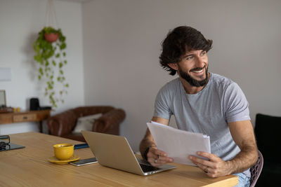 Man working at home in his kitchen with laptop and papers on wooden desk.  notebook . home office