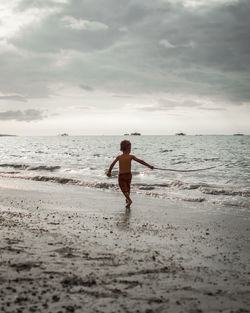 Rear view of shirtless man on beach against sky