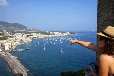 Side view of mature woman pointing towards sea while standing against blue sky