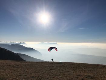 Person paragliding over landscape against sky