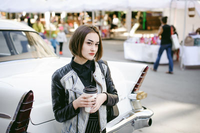 Beautiful woman having coffee while standing by car on road