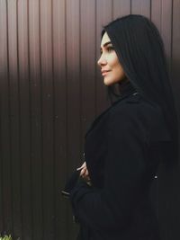 Side view of young woman standing by wall