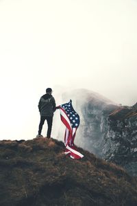 Rear view of man with american flag standing on mountain against sky