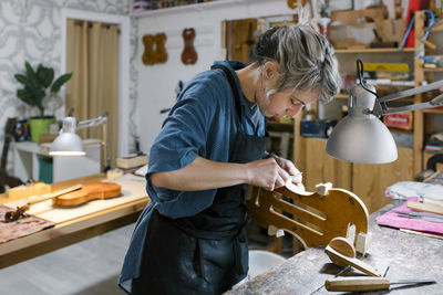 Luthier carving on violin at desk in workshop