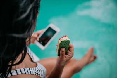 Midsection of woman holding mobile phone in swimming pool