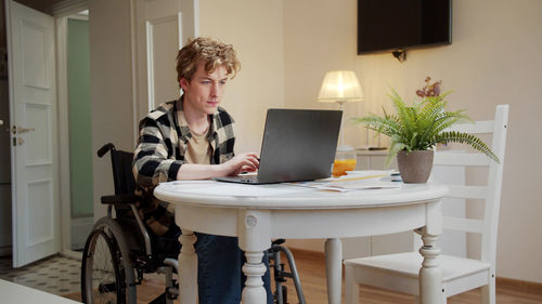 Young man sitting on wheelchair using laptop