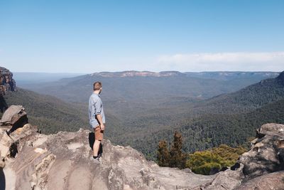 Rear view of man standing on rock against sky