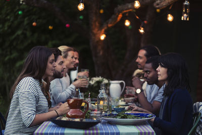 Side view of happy multi-ethnic friends having dinner at table in yard