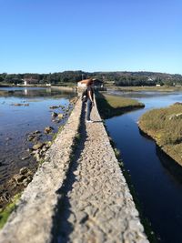 Side view of woman standing on walkway amidst river against clear sky