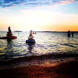 Silhouette people sitting on sea against sky during sunset