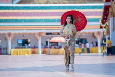 Woman wearing traditional clothing holding umbrella while walking on footpath