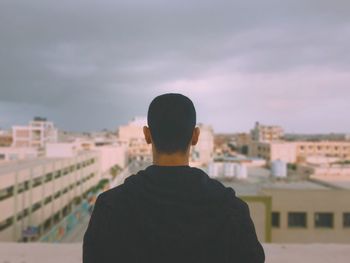 Rear view of man looking at cityscape against sky