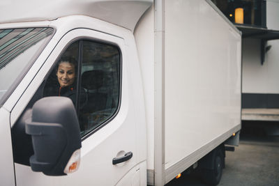 Smiling female worker driving white delivery van in city