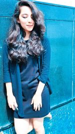 Young woman smiling while standing against blue wall