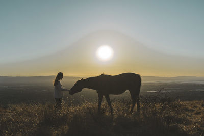 Silhouette man standing on field against sky during sunset