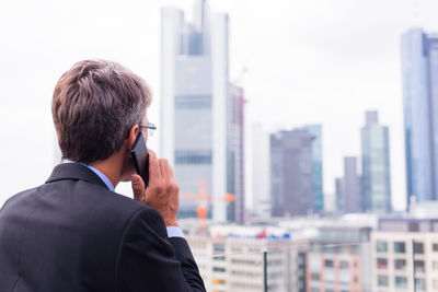 Rear view of man using mobile phone in city