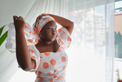 Portrait of beautiful young woman standing against window