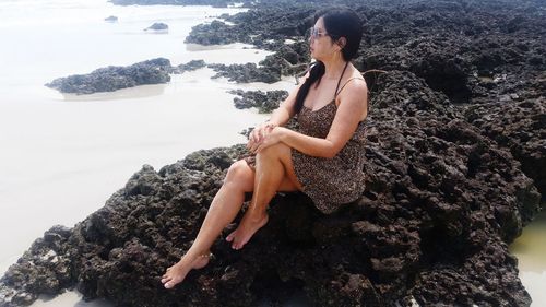 Mid adult woman sitting on rock formation by sea