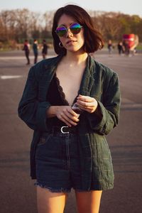Portrait of young woman wearing sunglasses while standing on road