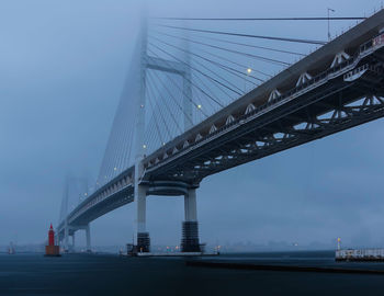 Low angle view of suspension bridge against sky on foggy morning in yokohama, japan.