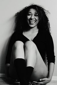 Portrait of cheerful young woman sitting against wall