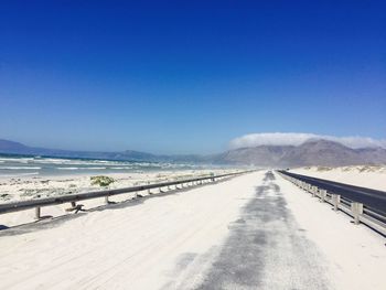 Road on snow covered landscape against clear blue sky