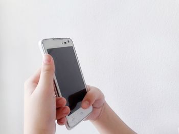Cropped hands of woman using mobile phone against wall