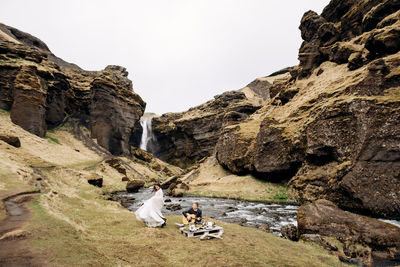 People sitting on rock by mountain against clear sky