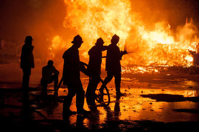 Silhouette firefighters spraying water on fire at night