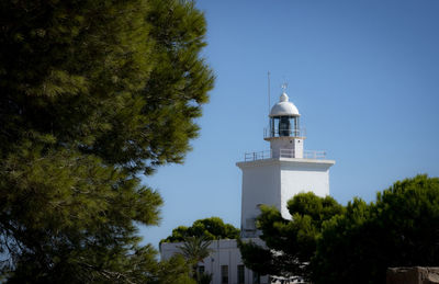 Low angle view of lighthouse amidst trees and building against sky