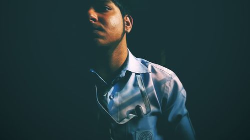 Portrait of young man standing against black background