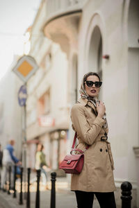 Portrait of fashionable woman in sunglasses standing against building in city